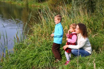 Fototapeta premium Mother with children sits on bank of pond