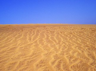 Sand in a wave pattern with a blue sky