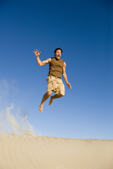 An attractive man jumping off a sand dune