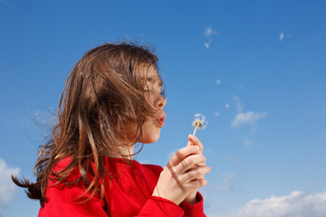 Girl blowing dandelion against blue sky