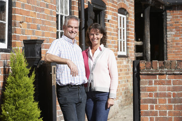 Farmer And Wife Standing In Front Of Farmhouse