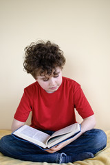 Boy reading book sitting on bed