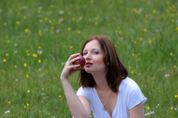 Pretty woman eating red apple on the summer glade