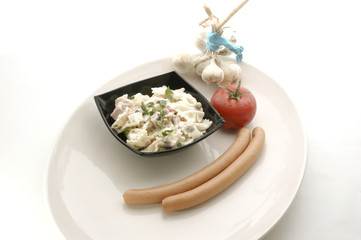 Nudelsalat in einer schwarzen Schale und Wuerstchen und Tomate