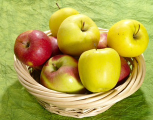 fresh juicy apples on green background in straw plate