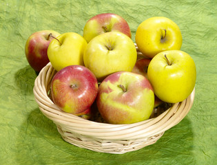 fresh juicy apples on green background in straw plate