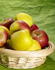wet juicy apples on green background in straw plate