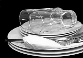 Pile of white plates, glasses with forks, spoons,silk napkin.