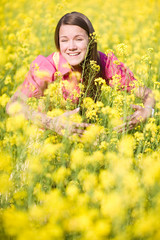 Pretty smiling girl relaxing on green meadow full of yellow flow