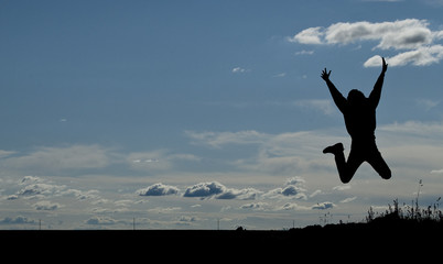 Silhouette of a young joyful man jumping on blue sky background