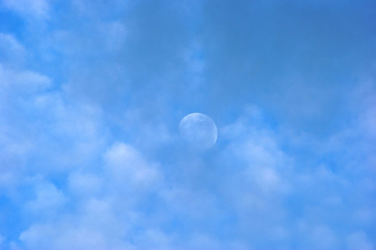 moon peeking out on an afternoon above the clouds