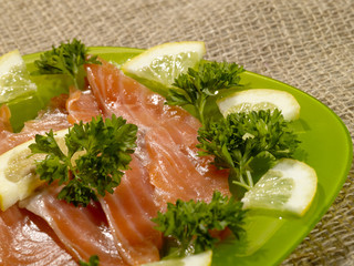 sliced salmon fish on the green plate with greenery and lemon