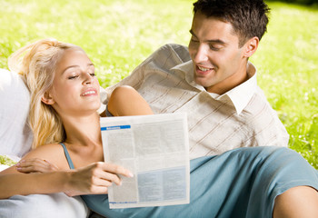 Happy smiling young couple reading together outdoors