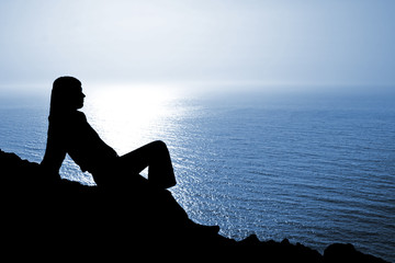 Sitting woman silhouette against deep blue seascape