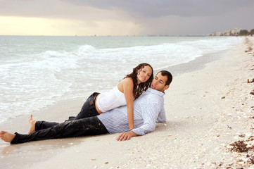 woman laying on top of man at beach looking at viewer