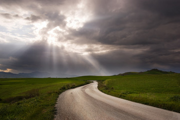 road crosses prairie covered by clouds into rays of sun