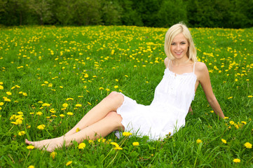 Young woman relaxing on a green meadow with dandelion