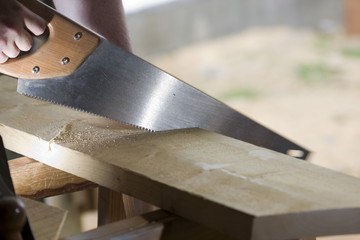 carpenter cuts a plank with a saw - obrazy, fototapety, plakaty