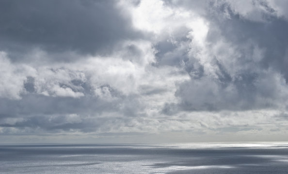 Silver clouds under shining sunlight above ocean with multiple shadows on the surface