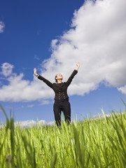 Fototapeta na wymiar Young woman standing in the grass towards blue sky
