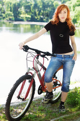 young girl with bicycle against blurred lake