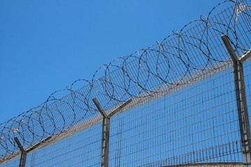 Fence with spiral barbed wire on top on sky background
