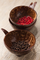 black and pink peppercorns in coconut bowls on old wooden table