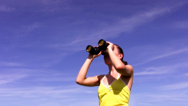 Woman looking through binoculars against the blue sky