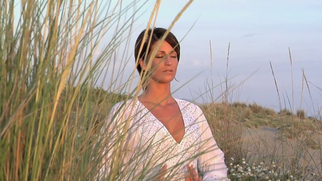 Donna medita in spiaggia con le mani giunte
