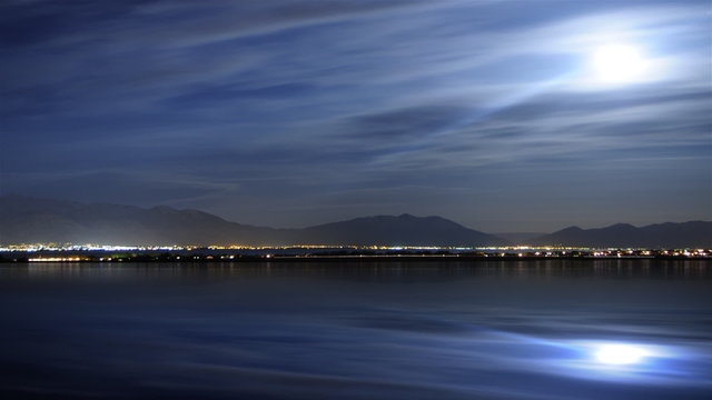 Moon clouds time-lapse with city lights and reflections in lake