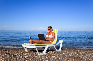 Sexy beautiful woman in bikini using laptop at the beach