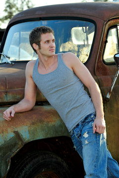 Rugged Male In Tank Top Leaning On Old Trucks