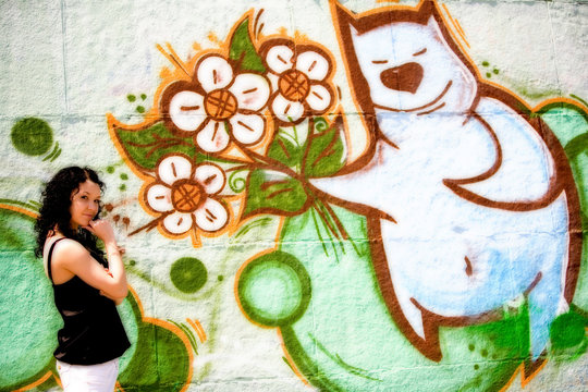 girl near the wall with graffiti bear-cub give flowers
