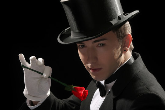 young magician performing red rose on black background