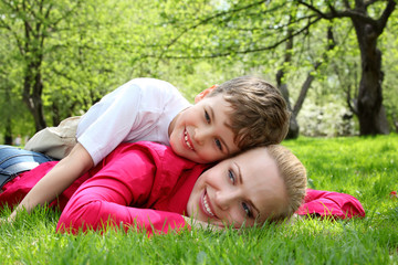 Fototapeta premium son lies on back of mother lying on grass in park in spring