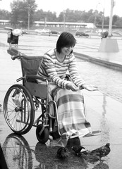 young woman in an invalid carriage feeds pigeons