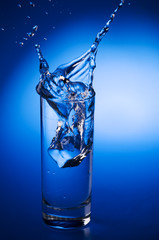 Mineral water splashing out from glass with ice cube.