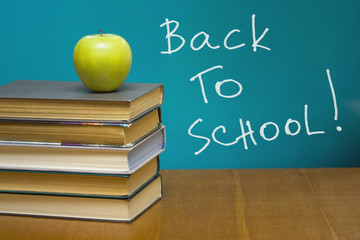 A green apple and  books on the desk. Blackboard with sign.