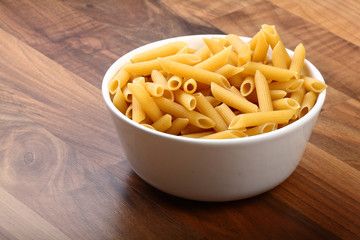 Dry penne rigate in white ceramic bowl on wooden floor