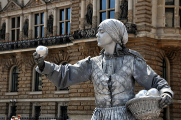 Die stillstehende Marktfrau auf dem Hamburger Marktplatz. Die Straßenkunst der Straßenkünstlerin als lebende Statue. Sie bietet Äpfel zum Kauf an,  Gesundheit.