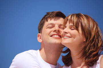 attractive pair against blue sky, touching by cheeks.