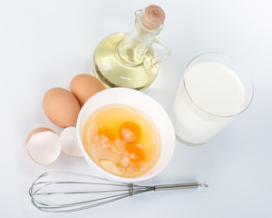 Fototapeta na wymiar Eggs, oil, cup of milk and whisk