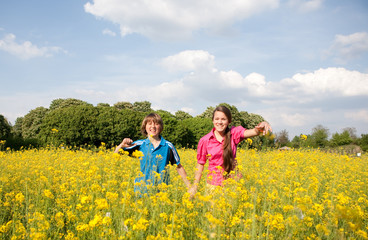 Girl and boy relaxing on meadow full of yellow flowers. Soft foc