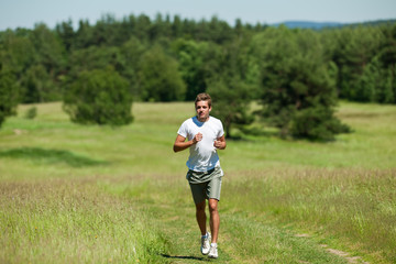 Young man with headphones jogging in a meadow