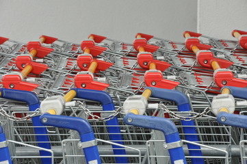 Die Einkaufswagen vor dem Discounter aneinandergekettet. Für den Wareneinkauf im Supermarkt stehen die Einkaufshilfen bereit. rot, blau, Detail