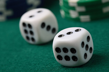 Pair of gambling die and poker chips on a green surface.