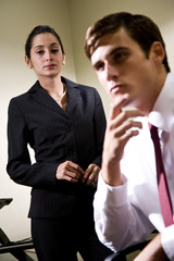 Pensive young businesswoman watching male colleague