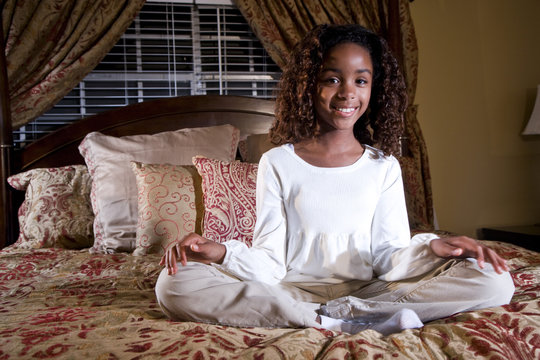 Cute 10 year old African American girl sitting on bed