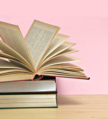 Open book and pile of books isolated on pink background