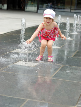 Happy beautiful girl playing with fountain in front of building